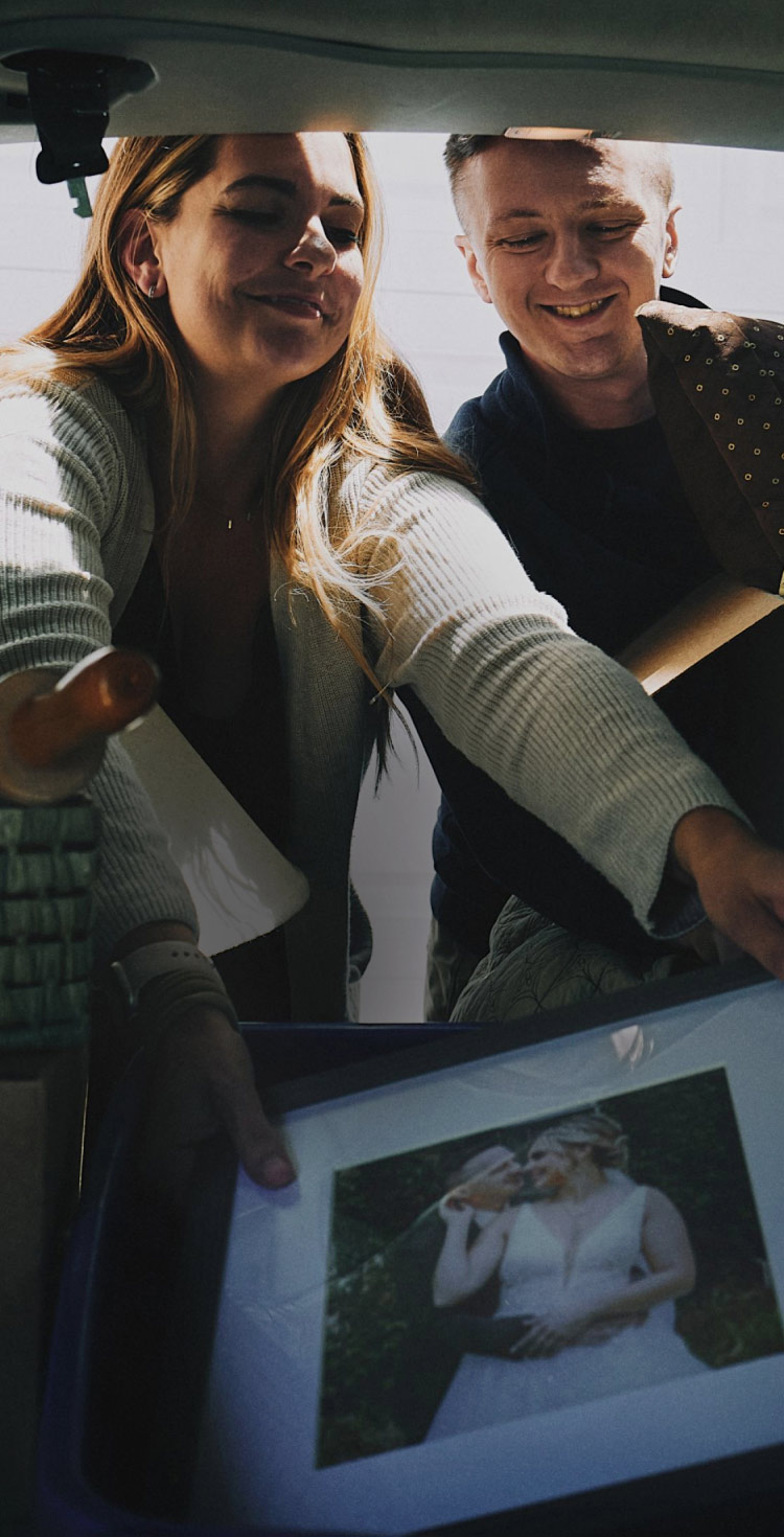 A husband and wife packing a framed photo of their wedding day into a trunk