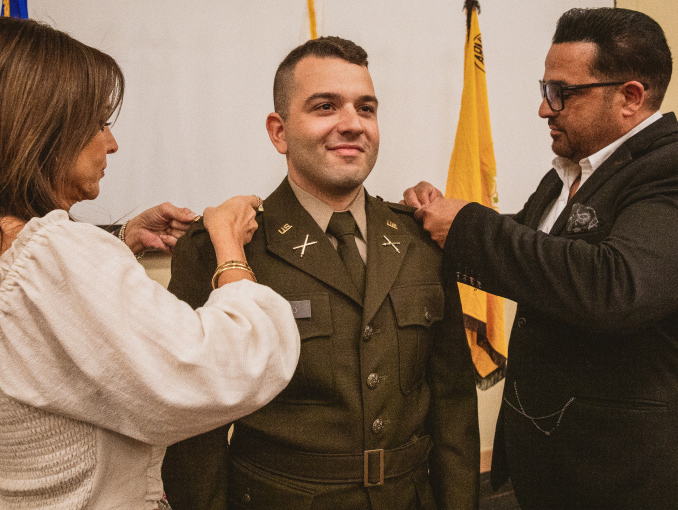 An Army Officer stands at attention while his parents pin his insignia on his shoulders during a commissioning ceremony