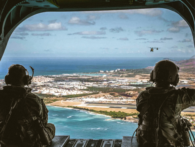 Two Aircraft Crewmembers looking out of a flying helicopter with the ocean in the background