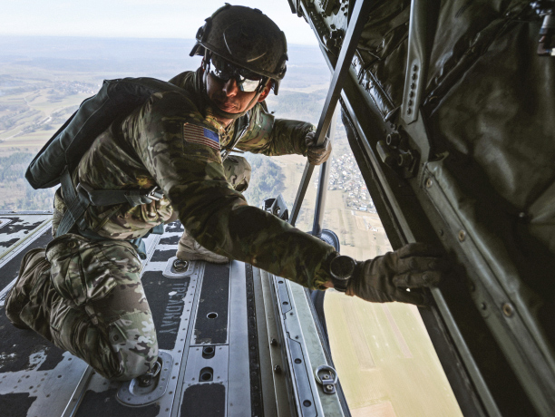 A Soldier in combat gear bracing himself on a flying helicopter