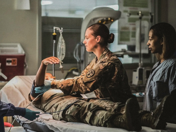 An Army medic attaches a blood pressure cuff to a patient in an emergency room