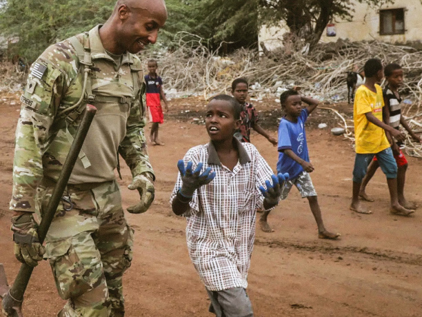 An Army Soldier speaks with children during a tree planting in a village