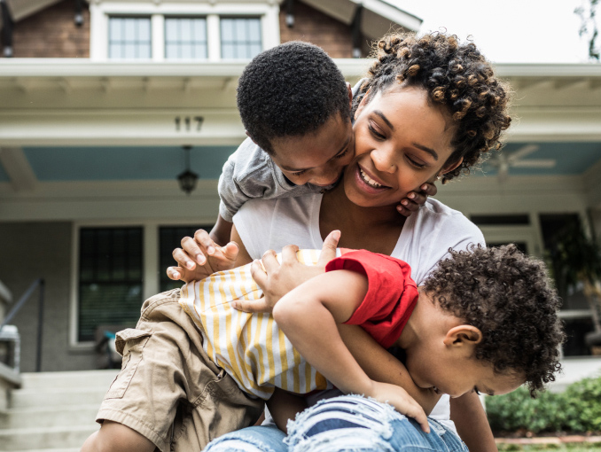 A mother and her two young sons playing in front of their house