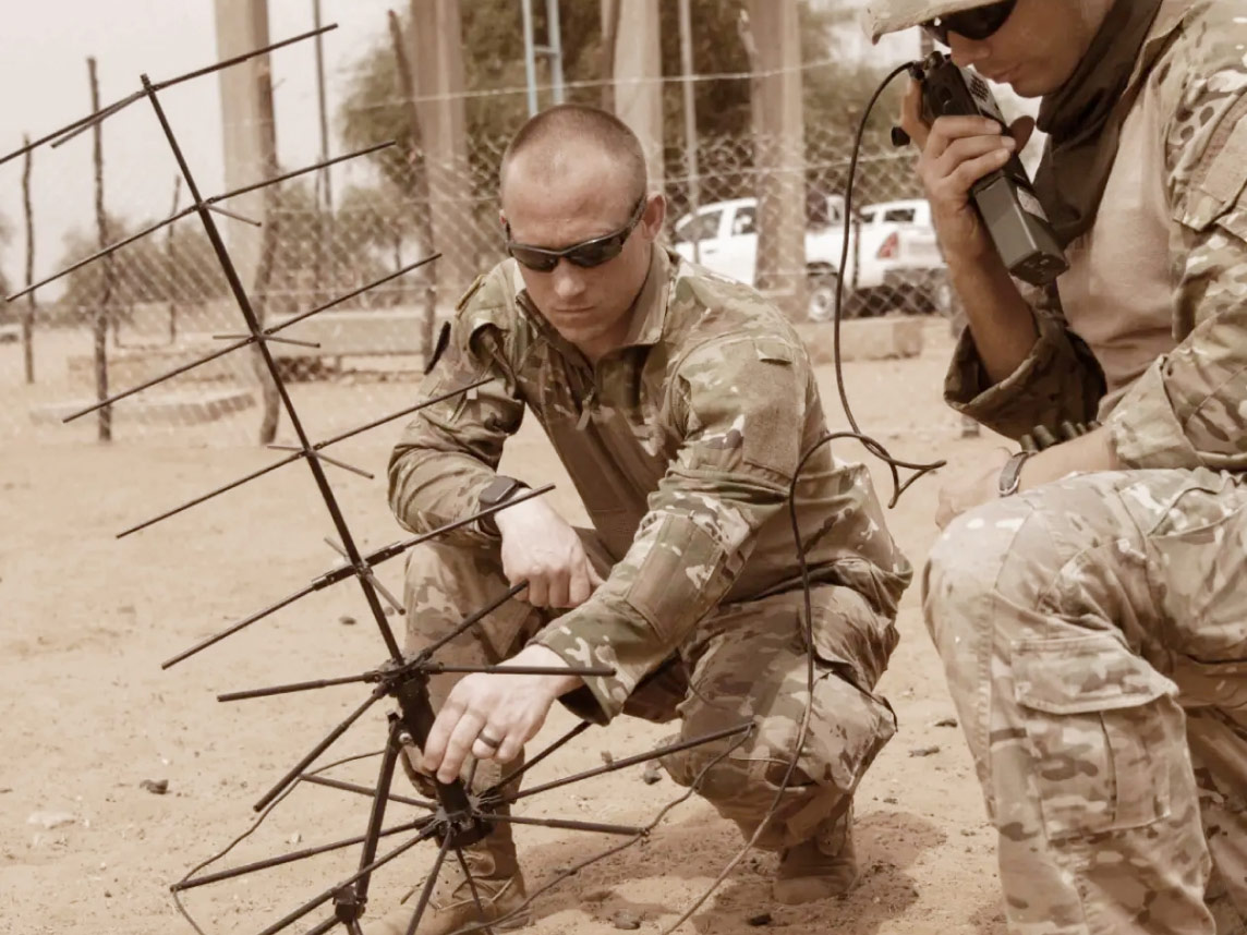 Two Psychological Operations Soldiers kneeling in sand setting up communications technology