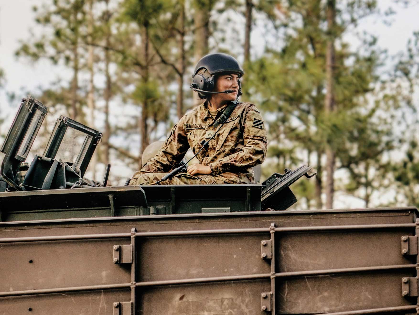 Soldier in uniform seated aboard a tank looking over her shoulder