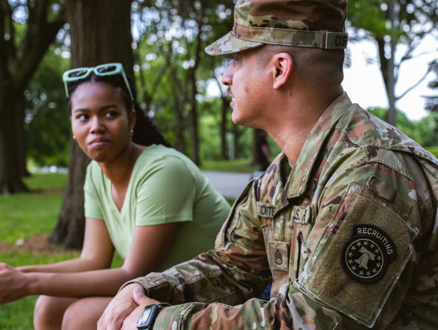 A male Army recruiter talking to a young female sitting on a bench outdoors