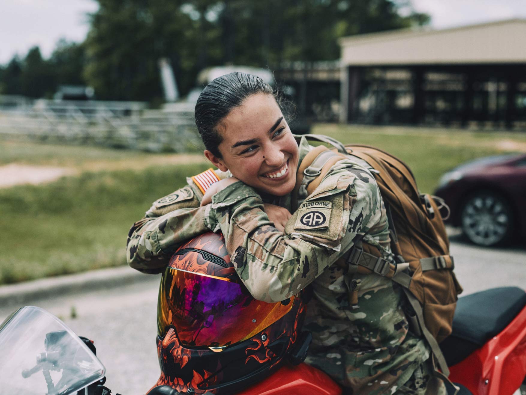 A smiling female Soldier in combat uniform siting on a motorcycle