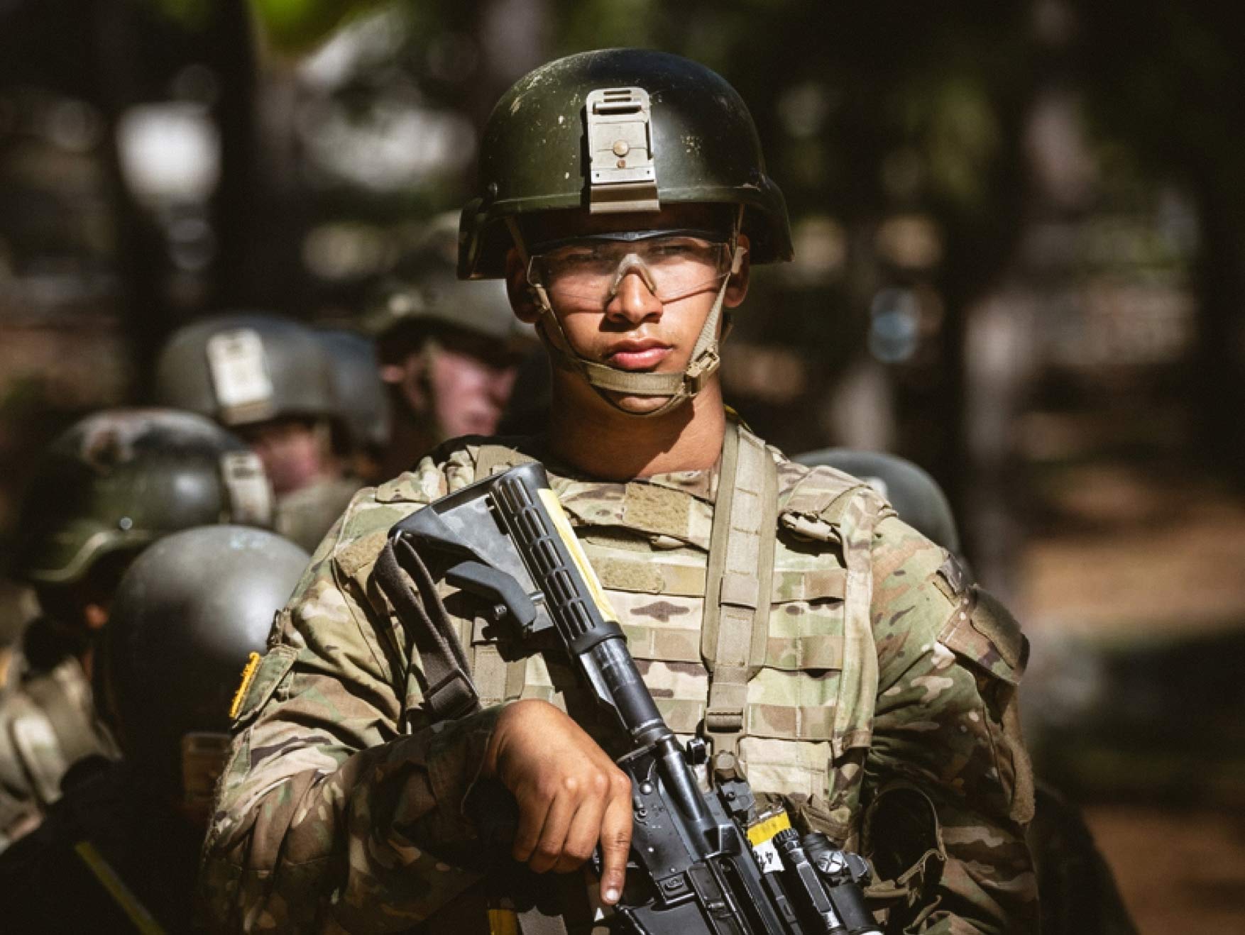 A trainee in combat uniform wearing a helmet and safety glasses holding a rifle during basic training