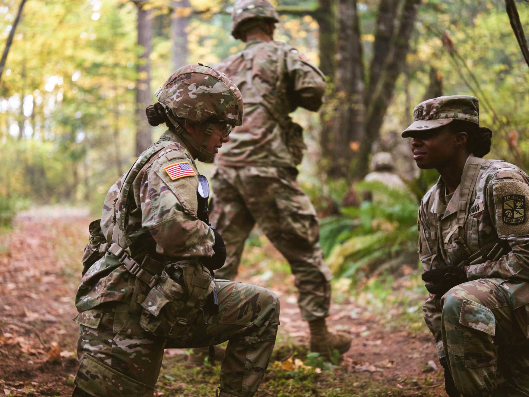 Two female Soldiers in combat uniform kneeling in a forest