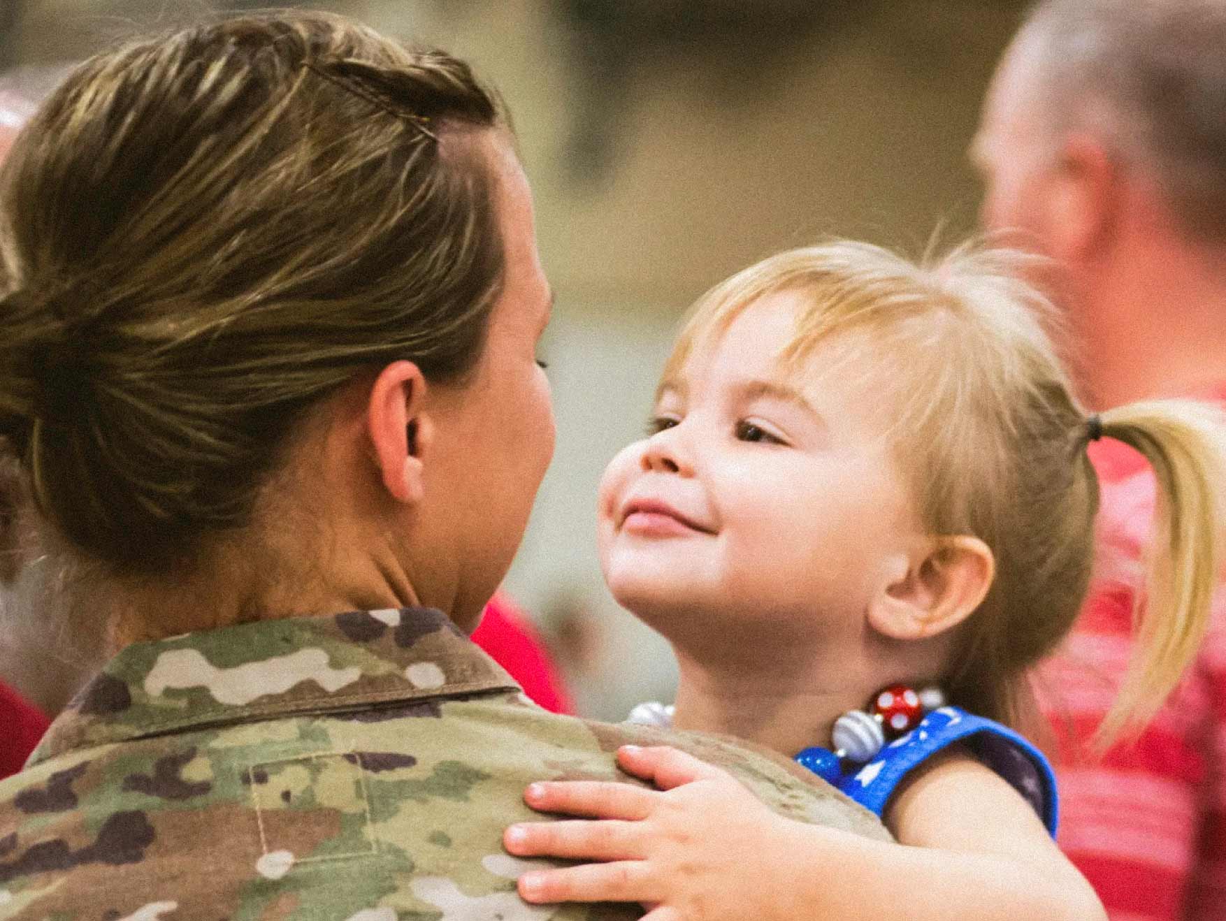 A female Soldier in combat uniform holding her toddler daughter