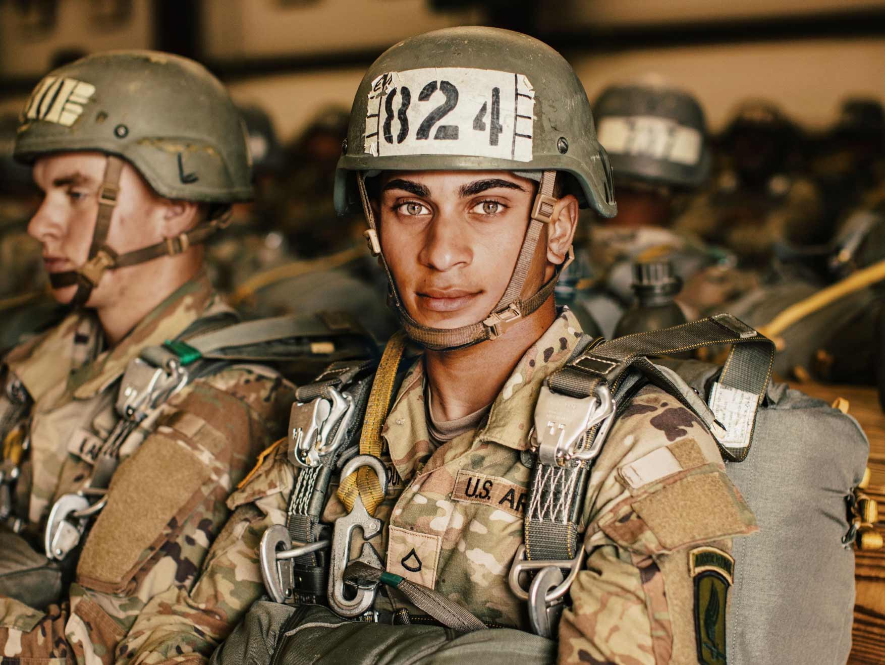 A Soldier in combat uniform and a helmet sitting in a vehicle with other soldiers